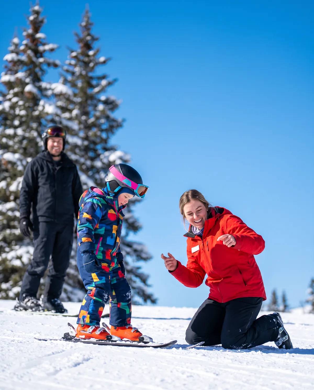 A ski instructor in a red jacket cheering on a young child during a beginner ski lesson